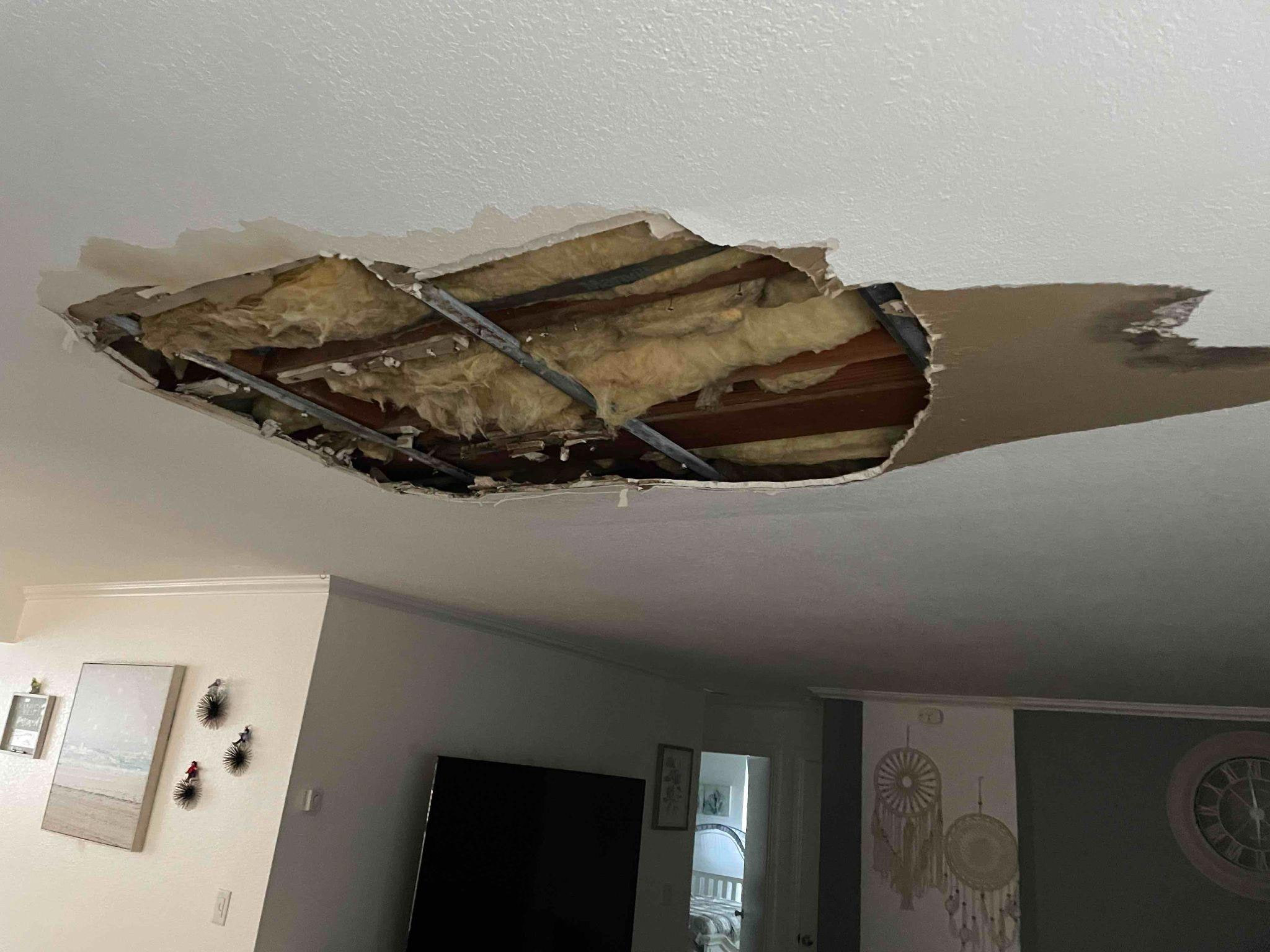 Large irregular opening in a living-room ceiling with insulation and framing visible